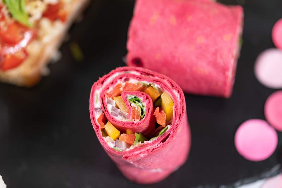 close up of Beetroot tortilla wrap, goats cheese mousse, bell peppers, red onions & rocket salad